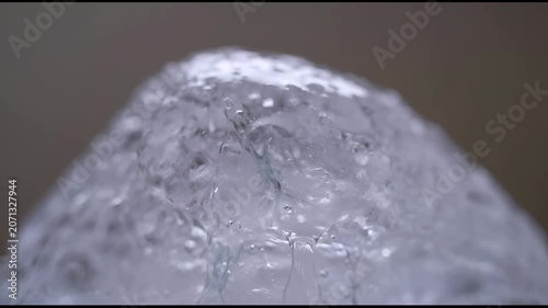 The video captures a close up view of water flowing over the surface of an ice cube or a similarly shaped transparent object