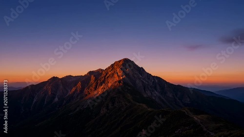 The sequence of images depicts a mountain landscape during different times of the day, showcasing a dramatic transition from sunset to night