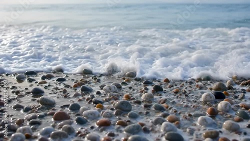 The video captures a tranquil scene at a pebble covered shoreline as gentle waves roll onto the beach