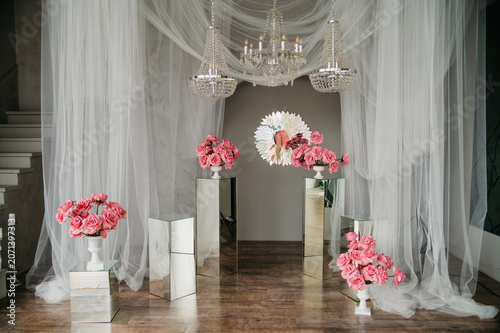 The photo studio is decorated with white transparent curtains and chandeliers with candles in the background of glass furniture, fresh flowers and a mirror on the wall