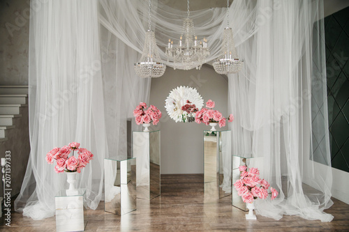 The photo studio is decorated with white transparent curtains and chandeliers with candles in a setting of glass furniture and fresh flowers