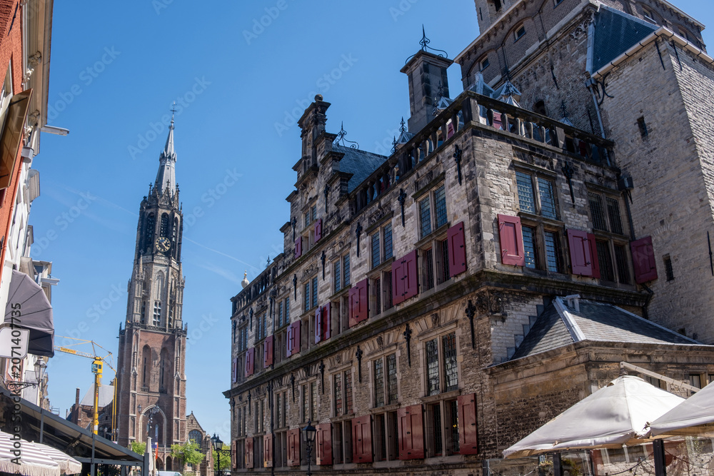 Obraz premium Nieuwe Kerk tower and historic stone facades in Delft city center under clear blue sky, Netherlands