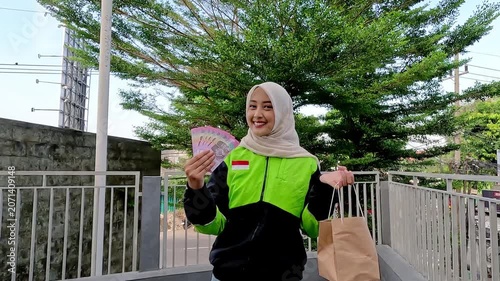 A young Muslim Asian woman, an online motorcycle taxi driver, is doing her job.