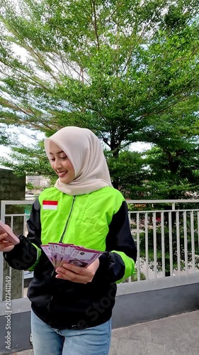 A young Muslim Asian woman, an online motorcycle taxi driver, is doing her job.