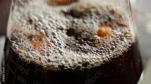 Macro closeup of carbonated dark soda with bubbles, fizzy beverage refreshment, drink texture and lively surface, ice in glass beaker, summer drink and science chemistry concept