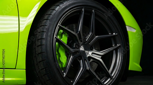 Close-up of a modern black alloy wheel on a bright green supercar with matching green brake calipers