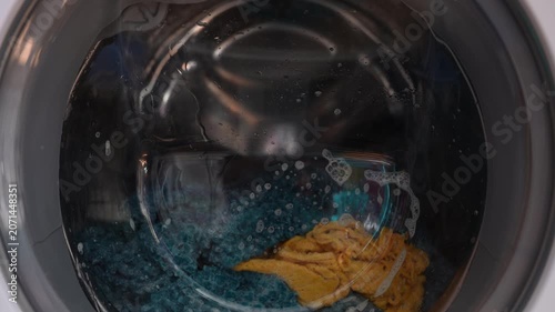 Clothing and soapy water spin around in machine. Washing machine door. Front loader