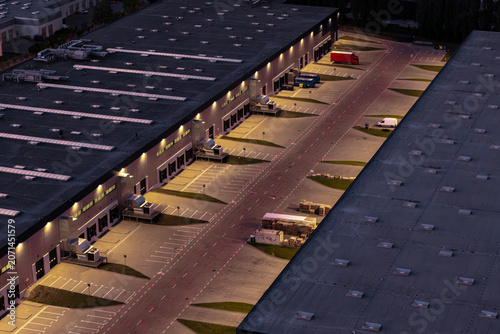 Aerial view of a logistics center at night with illuminated loading docks, warehouse buildings, and a parked truck in Warsaw, Masovian Voivodeship, Poland.