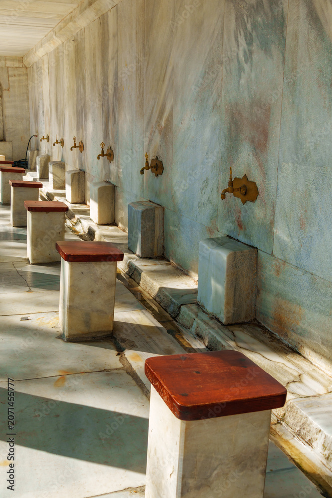 Naklejka premium Traditional Ottoman style marble ablution fountain with brass taps and stone seats in a historic mosque courtyard, Istanbul, Turkey architecture and culture concept.