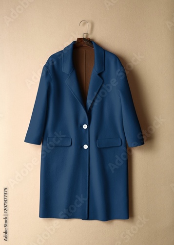 фотографія Blue long coat on a hanger against a beige background.