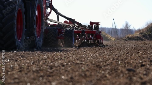 Low angle view shows large tractor and red multi disc cultivator cutting dry brown field, throwing dust and soil. Title appears. Utility pole and small vehicle sit near tree line.