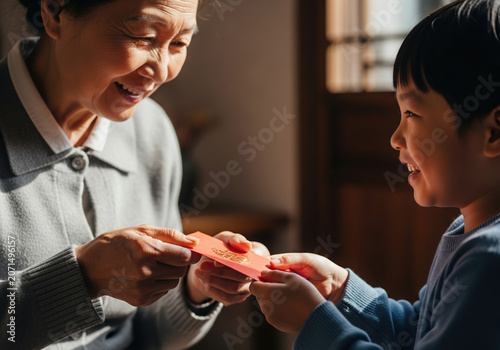 Asian grandmother giving red envelope to child with joy indoors  