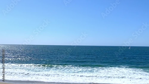 Panoramic view of the ocean and the beach with people walking along it.
