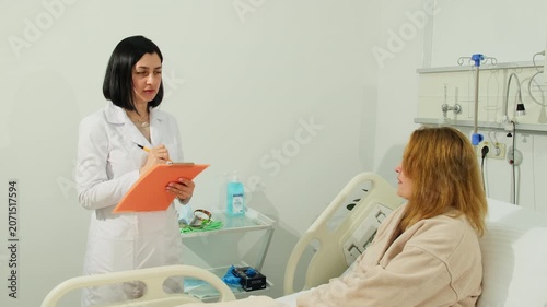 Doctor studies patient response during hospital consultation in bed. Physician writes observations on clipboard tracking treatment progress