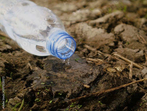 A clear plastic water bottle pouring water onto dry cracked earth with a blue cap in a close-up shot, conveying a dry
