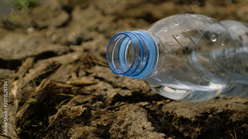 Close-up of discarded plastic water bottle on dry earth with blue cap