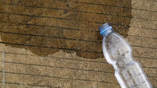Close-up of a discarded clear plastic water bottle on sandy bricks with a stain