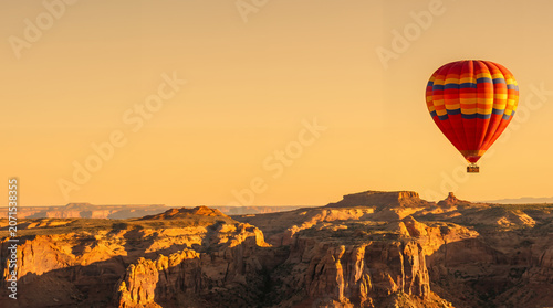 Colorful hot air balloon floating over a rugged desert canyon during sunset