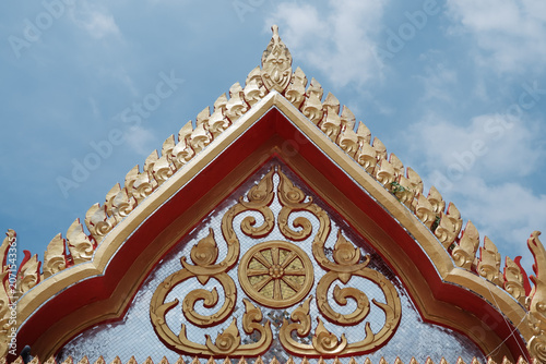 Obraz na plátně Intricate traditional Thai art and golden emblem on a mirror mosaic tympanum against blue sky