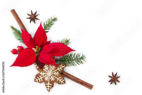 Christmas background with red poinsettia flower, gingerbread cookie, cinnamon sticks, anise stars, spruce branches and red berries on white background with copy space, top view