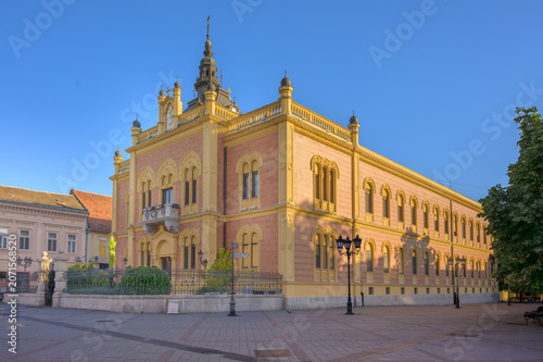 A vibrant cityscape of Novi Sad, Serbia, showcases historic European architecture under a clear blue sky.