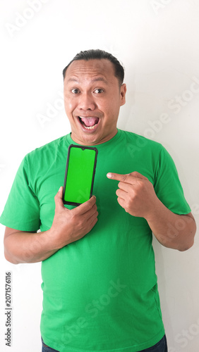 A portrait of a happy Asian man is smiling and showing copy space on his smartphone wearing green shirt isolated by a white background