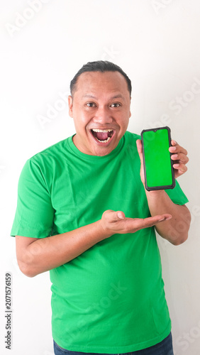 A portrait of a happy Asian man is smiling and showing copy space on his smartphone wearing green shirt isolated by a white background