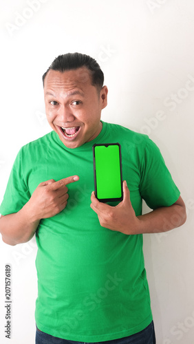 A portrait of a happy Asian man is smiling and showing copy space on his smartphone wearing green shirt isolated by a white background