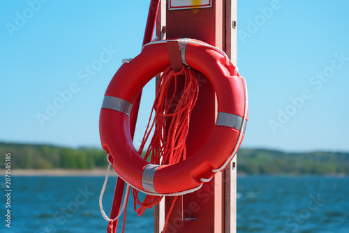 Schilderij op canvas Bright red lifebuoy hangs on marina post with 112 emergency sign, rope, and meta