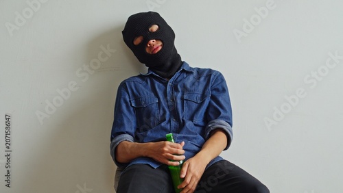 Photos Masked Criminal Holding A Bottle Sits Slumped Against A Wall