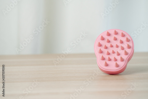 Soft pink silicone scalp massager brush with conical nubs on a wooden surface, shampoo massages, scalp exfoliation and improved circulation for gentle at-home hair care and bathing routines.