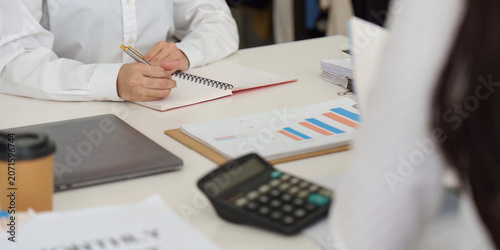Cropped hands writing in notebook at office desk with calculator and financial charts