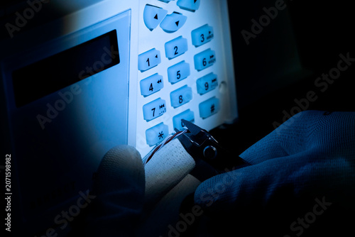 Obraz na plátne Man using tools to tamper with a security keypad at night in a dark room