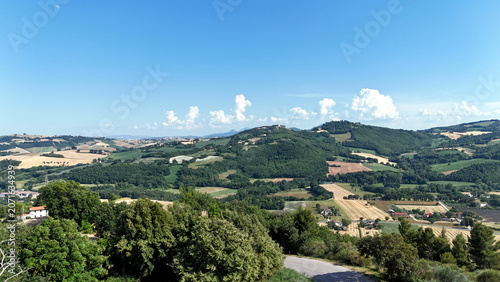 Panorama rurale con colline verdi, campi coltivati e cielo azzurro con nuvole sparse, in una scena naturale luminosa e tranquilla