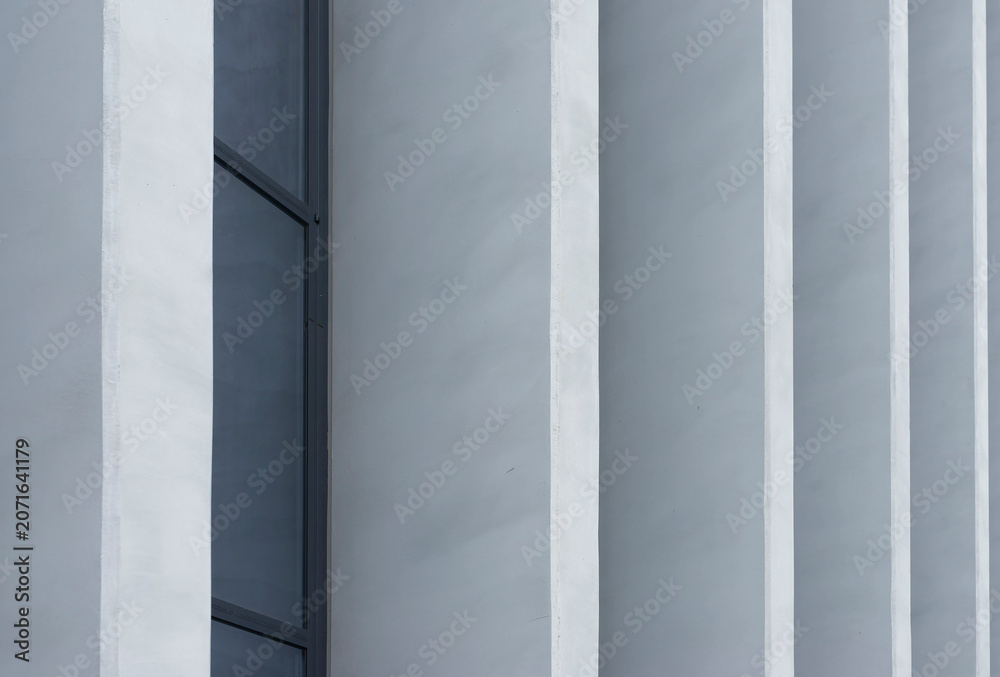 Naklejka premium Minimalist building facade with vertical white columns and a dark window strip. Gray architectural wall with clean lines and repeating surfaces.
