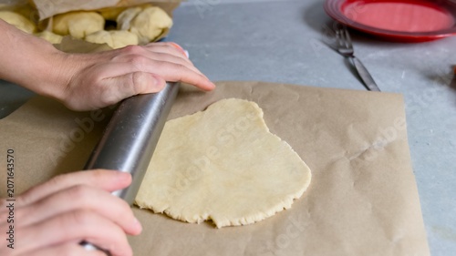 Hands flattening raw pastry dough on baking paper.