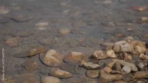Low-angle view of the Adriatic shoreline in Medulin, Croatia. Gentle waves wash over smooth pebbles as calm blue waters stretch toward the horizon. A peaceful summer coastal scene with a distant pier