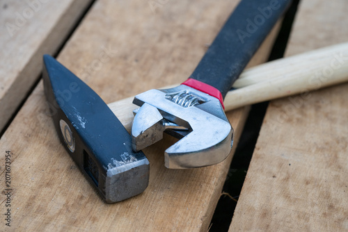 Fotografie a well-worn hammer with a wooden handle and a metal adjustable wrench rest crosswise on top of rough wooden pallet boards