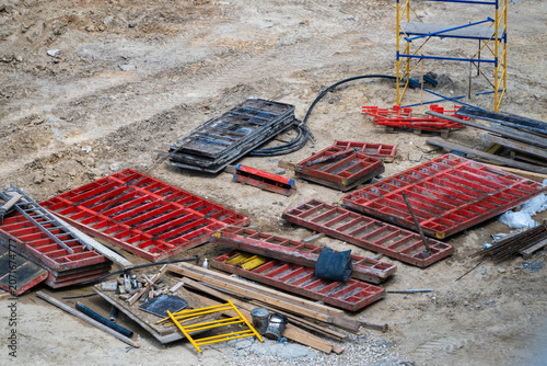Bild auf Leinwand a construction site features a collection of scattered red metal formwork panels, wooden boards, and various building supplies resting on the dirt ground near a yellow scaffolding tower