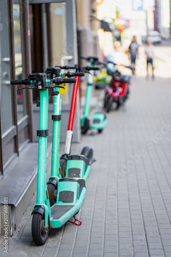 Obraz na plátně Row of shared electric scooters parked on a paved urban sidewalk representing mo