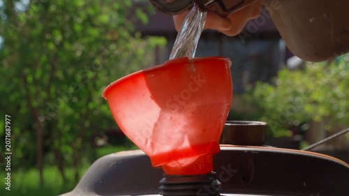 Pouring gasoline into lawn mower tank close-up. Preparing for lawn mowing