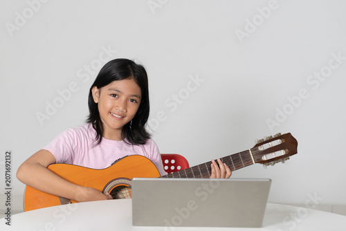 Smiling Young Asian Girl Learning to Play Acoustic Guitar with Laptop Online Lesson