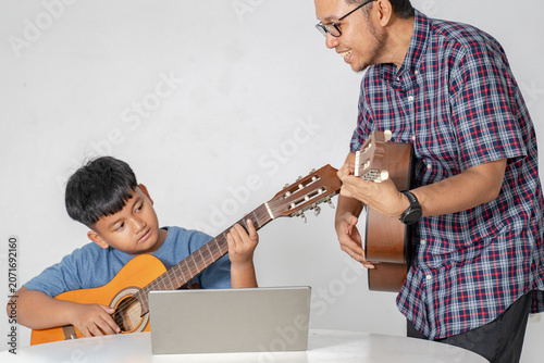 Asian Father Teaching His Young Son to Play Acoustic Guitar at Home