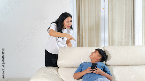 Angry Asian Mother Scolding Her Son for Overusing Smartphone on Sofa