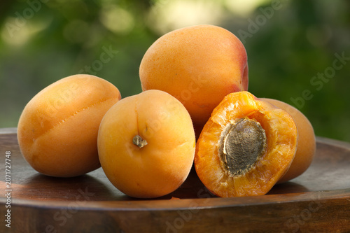 Fresh ripe apricots piled on a wooden plate with a blurred green background