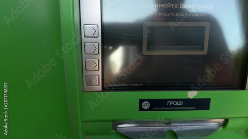 Close-up of a person withdrawing paper money from a green automated teller machine. The concept illustrates financial technology, digital banking, and economic independence