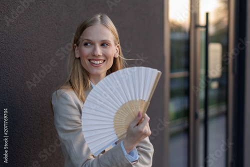 Young businesswoman cools down with a fan during summer heat near an office building