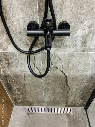 Fotografie Shower hose mount assembly with flexible tubing, black frame, gray marble tile w