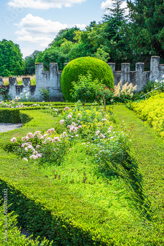 Garden scene with green bushes and flowers in a well-maintained landscape surrounded by a stone wall on a sunny day