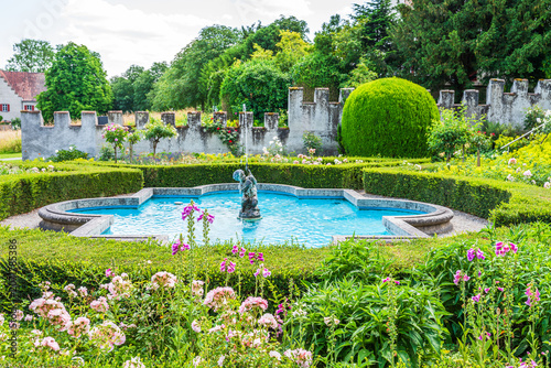Historic garden with a fountain and greenery near a lake on a sunny day in a rural setting